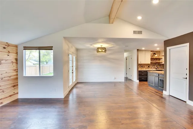 an empty room with wooden floor kitchen view and a window