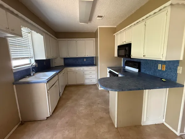 a kitchen with granite countertop a sink a stove top oven a counter space and cabinets