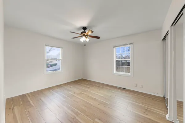 an empty room with wooden floor chandelier fan and windows