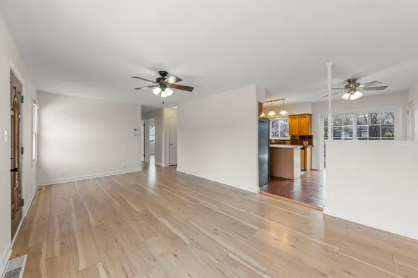a view of an empty room with wooden floor and a kitchen