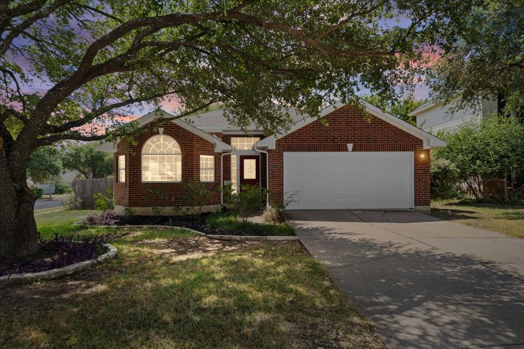 Mature trees shade a classic brick exterior complete with a two-car garage and paved driveway.