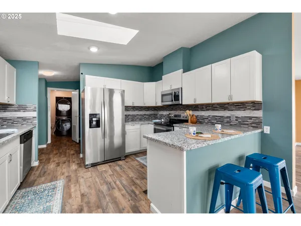 a kitchen with granite countertop a refrigerator a stove a sink dishwasher and white cabinets with wooden floor