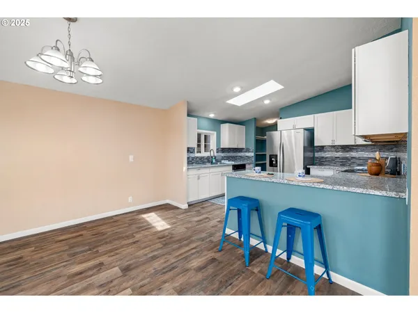 a open kitchen with stainless steel appliances granite countertop a refrigerator a stove a sink dishwasher and white cabinets with wooden floor