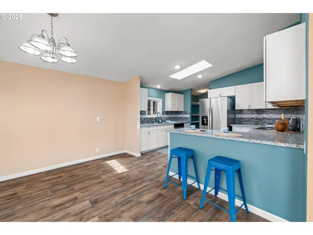 a open kitchen with stainless steel appliances granite countertop a refrigerator a stove a sink dishwasher and white cabinets with wooden floor