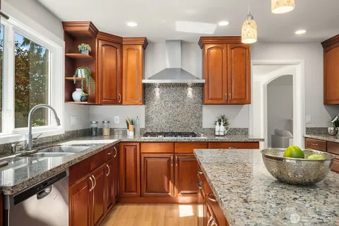 a kitchen with stainless steel appliances granite countertop a sink a stove and a wooden cabinets