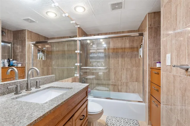 a bathroom with a granite countertop sink a toilet a mirror and shower