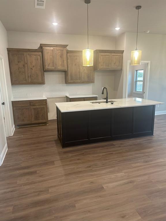 F1201 Sanger Drive Springtown, TX 76082 - Photo 10 of 11 Kitchen featuring decorative light fixtures, dark wood-type flooring, light stone countertops, an island with sink, and brown cabinetry