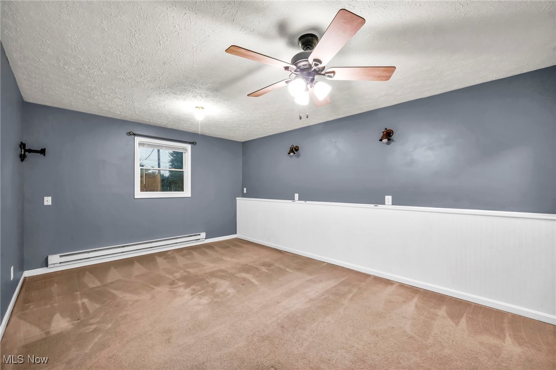 47655 Cooper Foster Park Road Amherst, OH 44001 - Photo 22 of 49 Spare room with a textured ceiling, baseboard heating, ceiling fan, carpet flooring, and a wainscoted wall