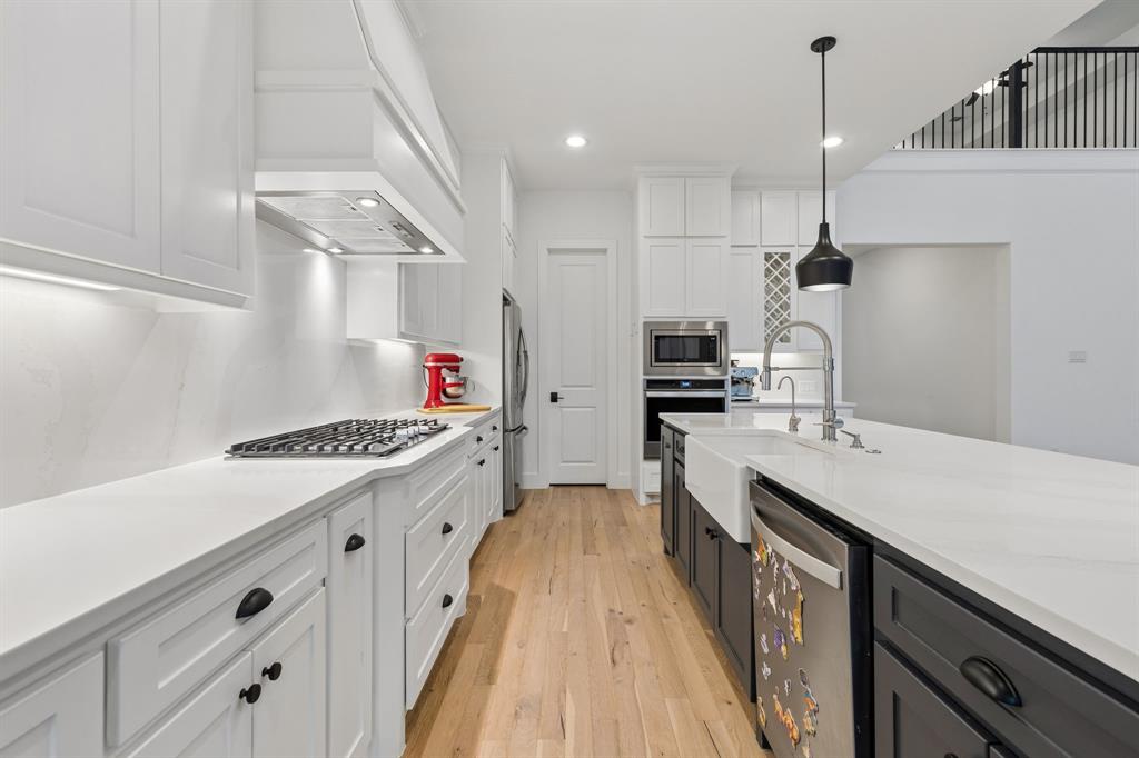 566 Broadleaf Way Haslet, TX 76052 - Photo 15 of 38 Modern kitchen featuring a gas cooktop, white perimeter cabinetry with black hardware, a large central island with a farmhouse sink, stainless steel appliances, and light wood-finish flooring