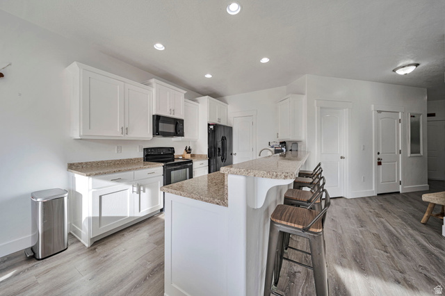 11730 South Shadow Lane Draper, UT 84020 - Photo 7 of 24 Kitchen with white cabinetry, a breakfast bar, black appliances, light wood-style flooring, and a peninsula