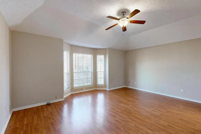 a view of an empty room with wooden floor and a ceiling fan