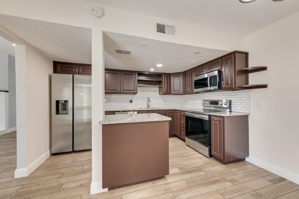 219 West Rochelle Road Irving, TX 75062 - Photo 9 of 29 Kitchen featuring wood-finish flooring, dark wood cabinetry, white subway tile backsplash, and stainless steel appliances