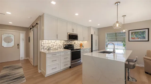 a kitchen with stainless steel appliances granite countertop a refrigerator a stove top oven a sink dishwasher and white cabinets with wooden floor