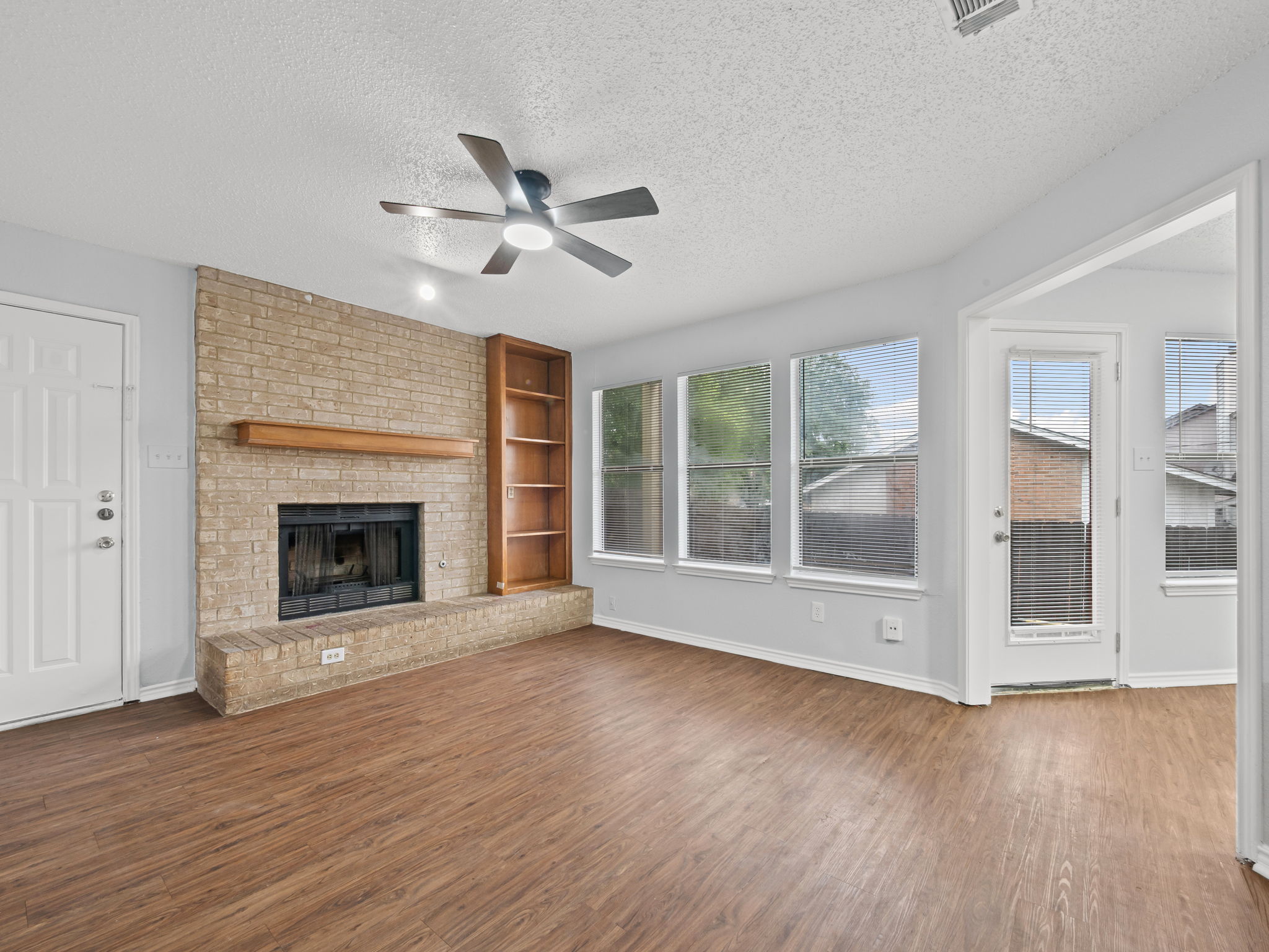 1816 Rawhide Loop, Unit 1822 Round Rock, TX 78681 - Photo 3 of 17 Unfurnished living room with a textured ceiling, ceiling fan, wood finished floors, healthy amount of natural light, and a fireplace