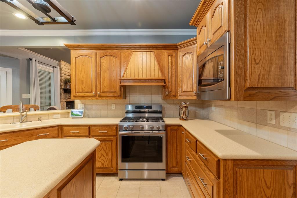 320 Rustic Oaks Road Combine, TX 75159 - Photo 15 of 40 Kitchen featuring appliances with stainless steel finishes, custom exhaust hood, crown molding, light countertops, and brown cabinets