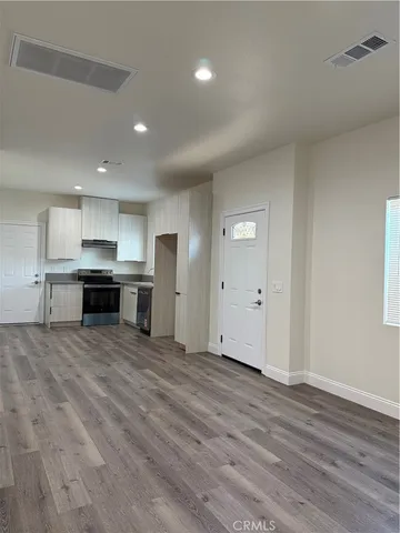 an empty room with wooden floor kitchen view and windows