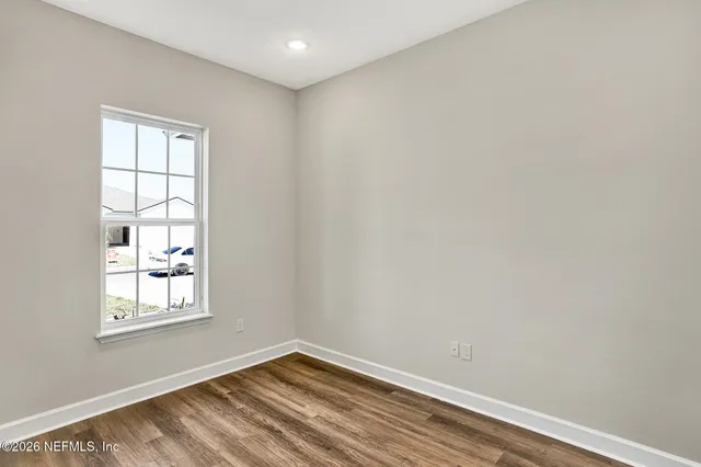 a view of an empty room with wooden floor and window