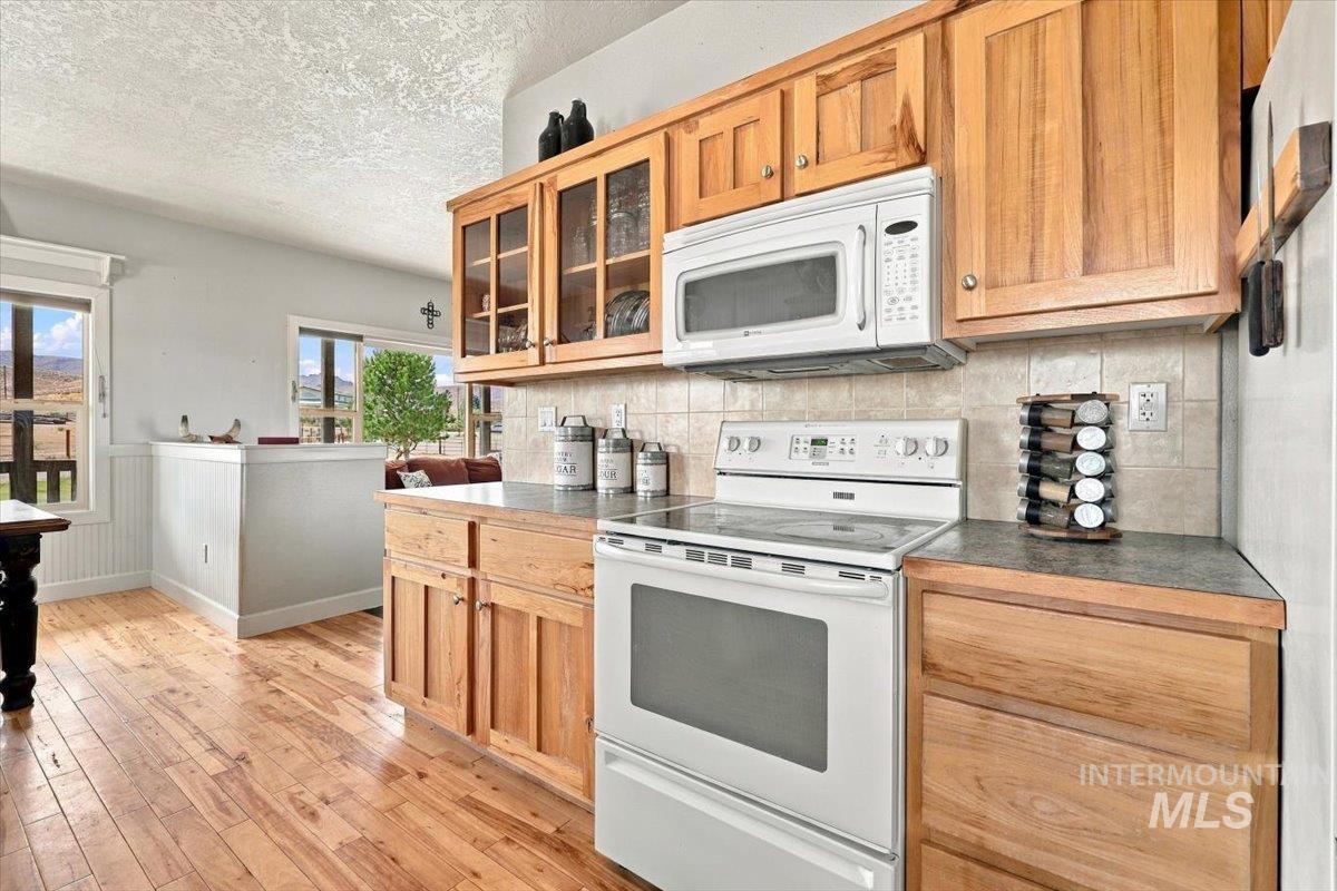 18026 Briar Creek Road Murphy, ID 83650 - Photo 16 of 50 Wood-finish flooring, wood cabinetry, tile backsplash, built-in dishwasher, and a window above the sink