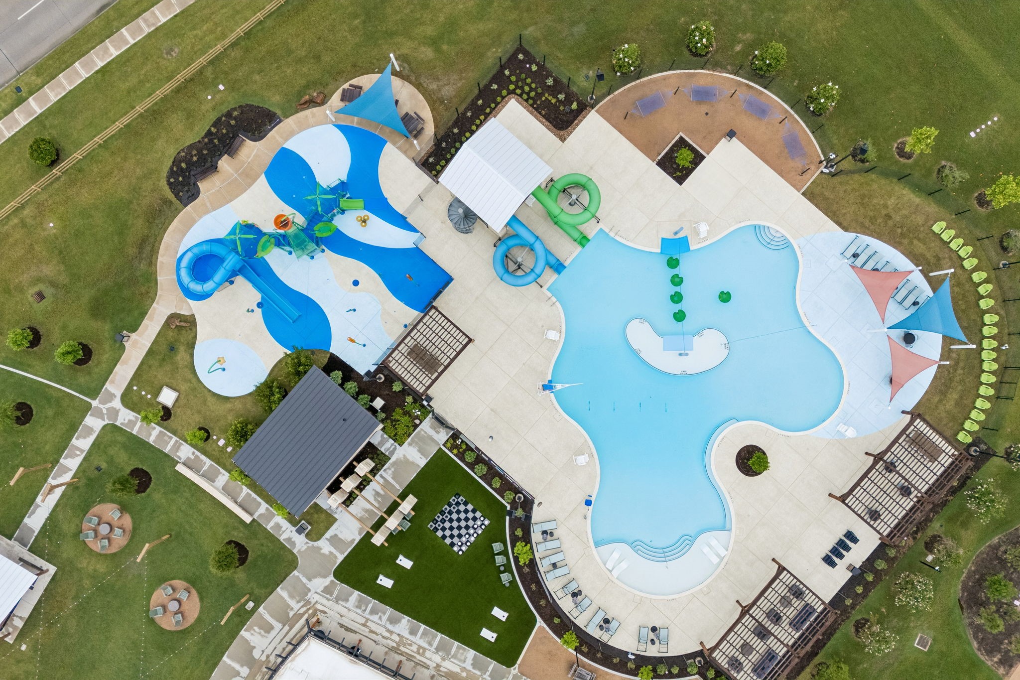 10902 Bonfire Trail Beasley, TX 77417 - Photo 31 of 36 This aerial photo showcases a vibrant community pool area with a large, uniquely shaped swimming pool, a children's splash pad with slides, shaded seating areas, and a nearby green space with pathways. Ideal for-friendly relaxation and outdoor activities.