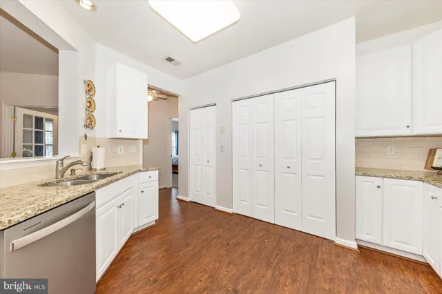 a large white kitchen with granite countertop a sink and dishwasher a stove with wooden floors