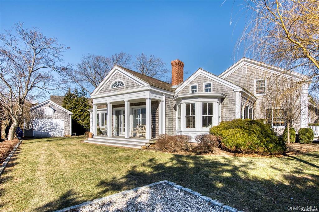 Back of house featuring covered porch, a chimney, a yard, and an outbuilding