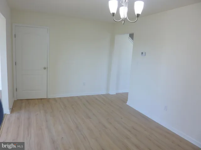 a view of an empty room with wooden floor and a chandelier
