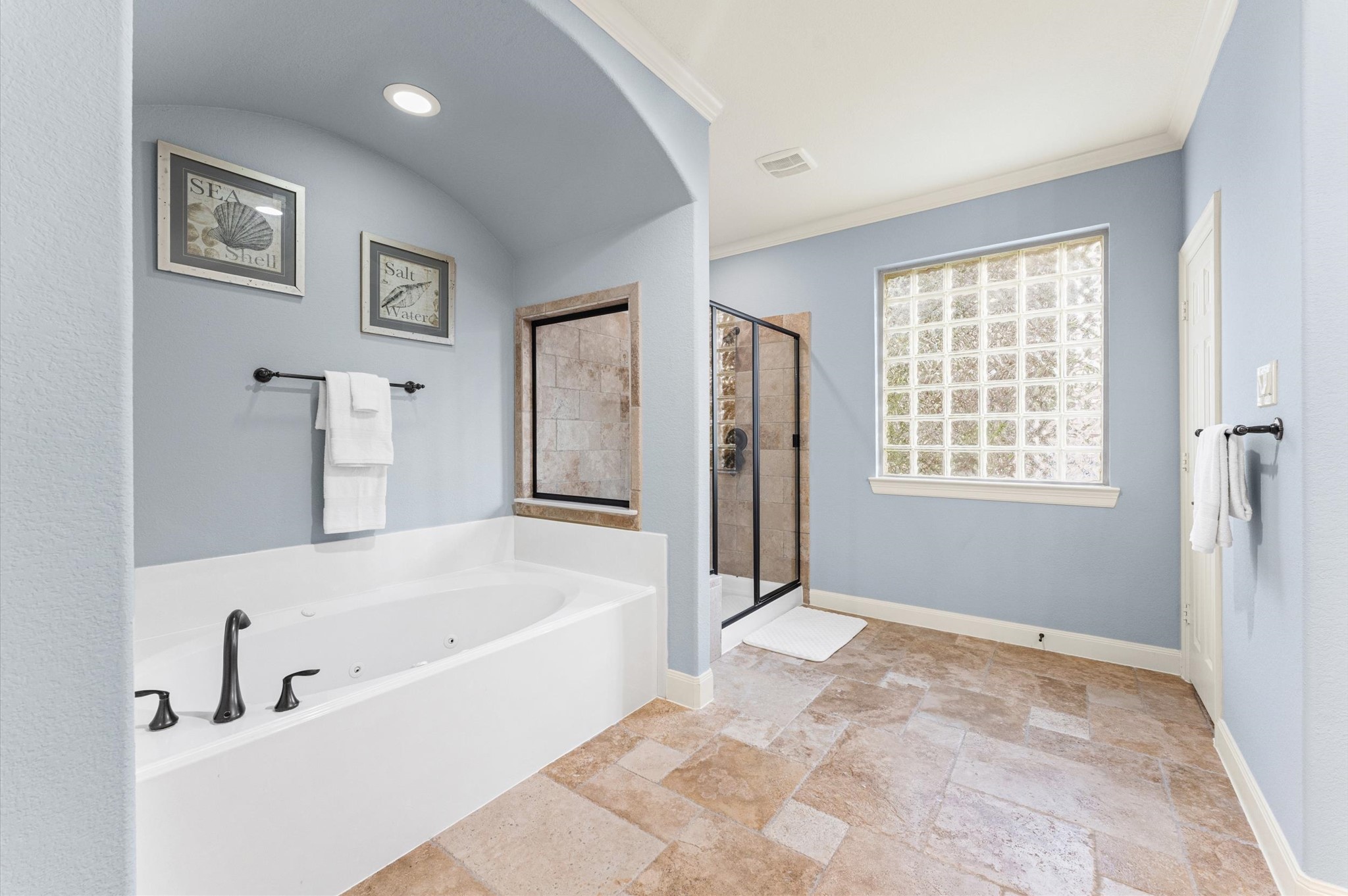 70 Valera Ridge Drive Spring, TX 77389 - Photo 34 of 37 Spacious bathroom with elegant blue walls, featuring a large soaking tub, separate glass-enclosed shower, and natural light through a glass block window, creating a bright and relaxing atmosphere.