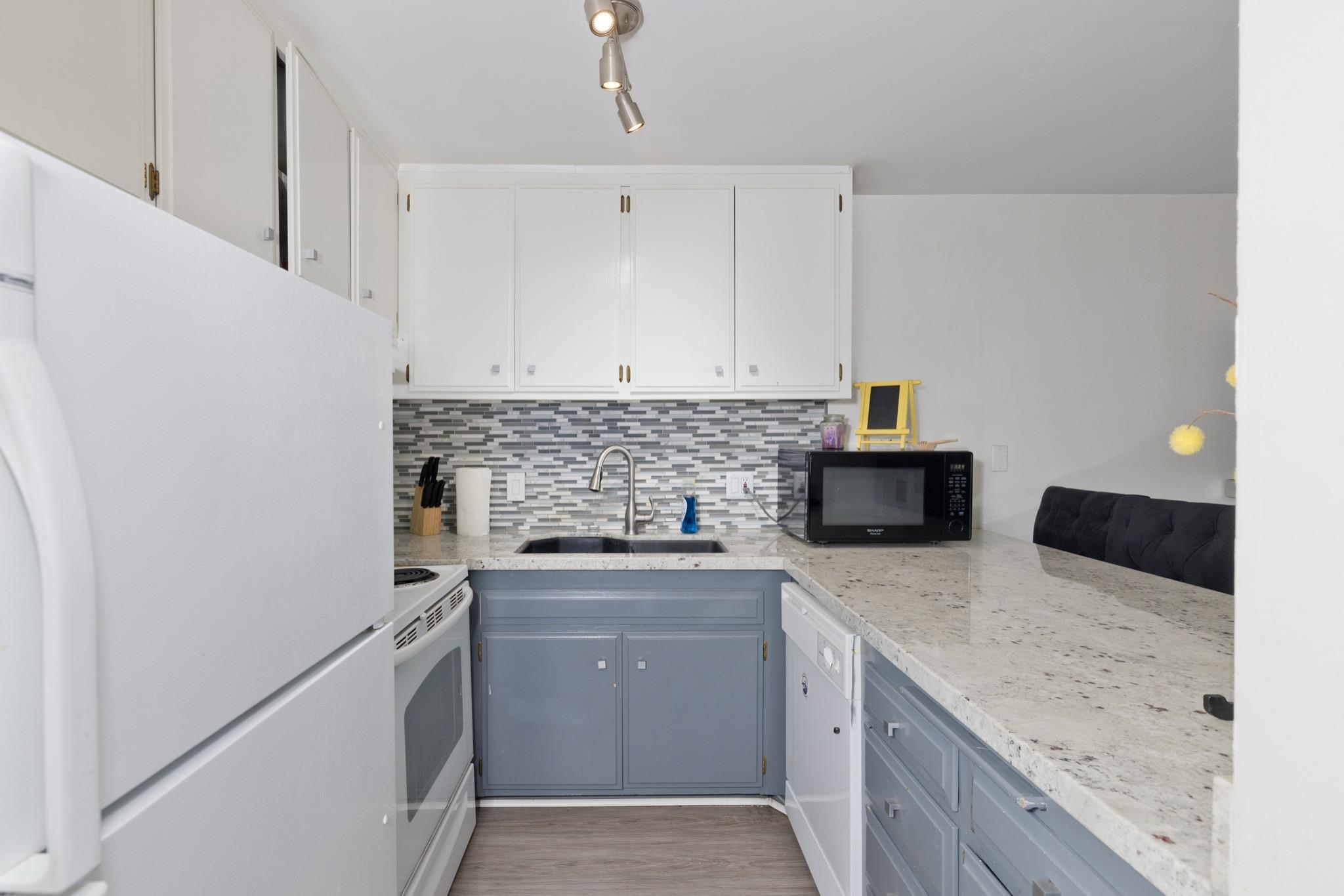165 Old Mammoth Road, Unit 13 Mammoth Lakes, CA 93546 - Photo 11 of 23 U-shaped kitchen featuring white upper cabinetry, gray lower cabinetry, light-colored granite-style countertops, a mosaic tile backsplash, and wood-finish flooring