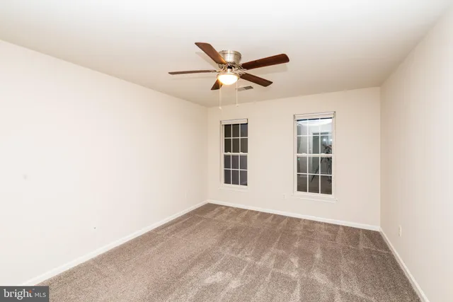 an empty room with chandelier fan and windows