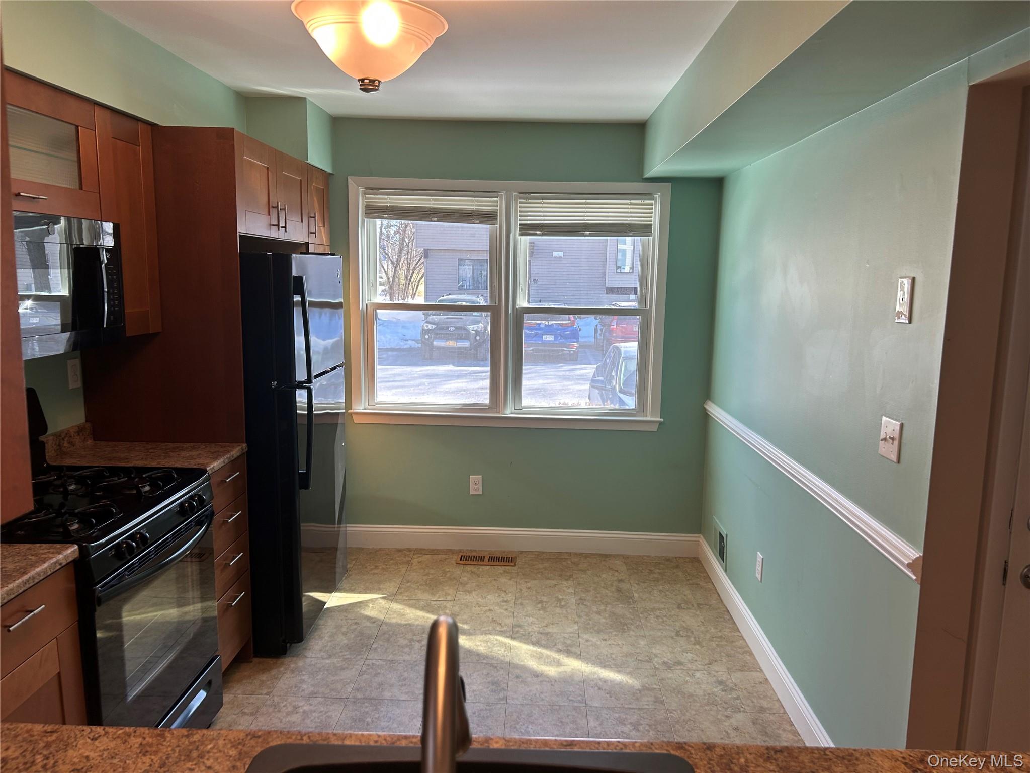 135 West Nyack Road, Unit 111 Nanuet, NY 10954 - Photo 6 of 16 Kitchen with black appliances, light tile patterned floors, wood finish cabinetry, glass fronted cabinets, and dark stone counters