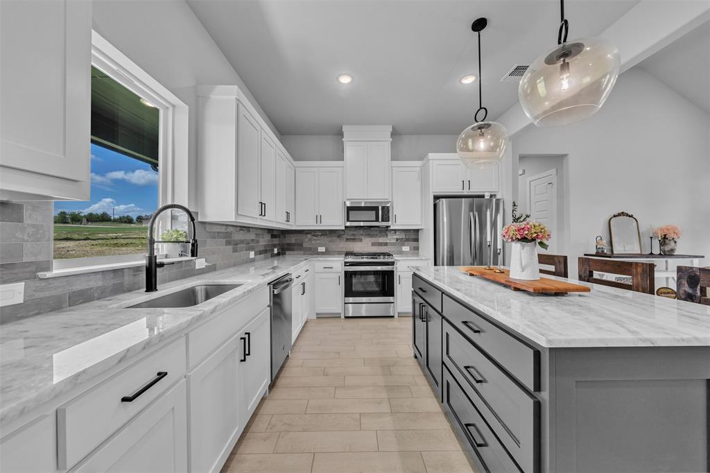 2004 Willy Dilly Road Springtown, TX 76082 - Photo 14 of 40 Modern kitchen featuring white shaker cabinetry, stainless steel appliances, a large center island with a stone countertop, a tile backsplash, and wood-finish flooring