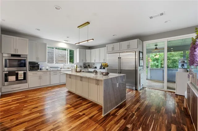 a kitchen with stainless steel appliances granite countertop a refrigerator a sink dishwasher a stove and white countertops with wooden floor