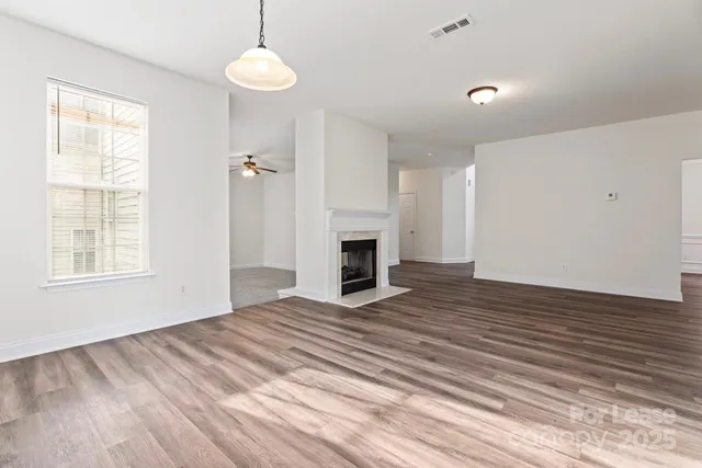 a view of an empty room with wooden floor fireplace and a window