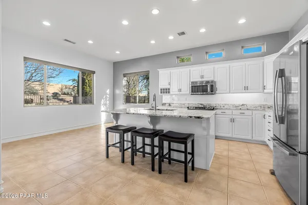 a kitchen with kitchen island granite countertop a stove a sink a refrigerator and white cabinets with wooden floor