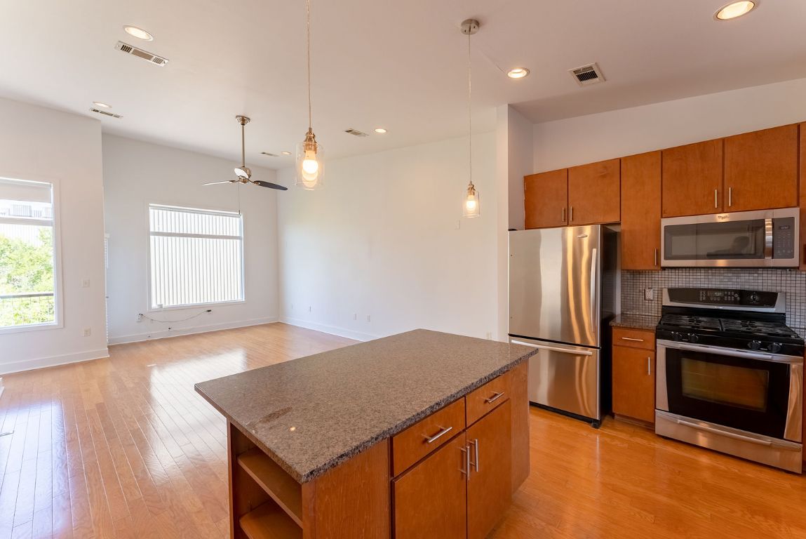 1702 South Lamar Boulevard, Unit 27 Austin, TX 78704 - Photo 7 of 20 Kitchen featuring appliances with stainless steel finishes, brown cabinets, a center island, open shelves, and decorative light fixtures