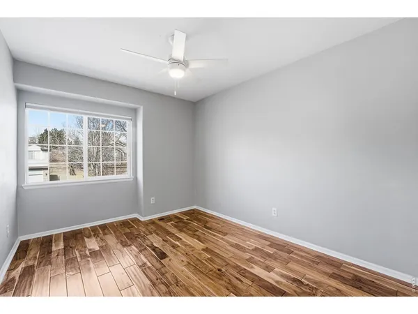 an empty room with wooden floor chandelier fan and windows