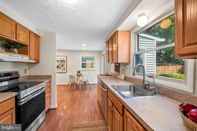 a kitchen with stainless steel appliances granite countertop a sink a stove top oven a chimney cabinets and a dining table