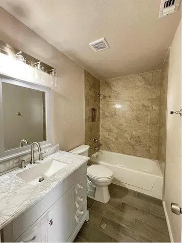 a bathroom with a granite countertop sink a toilet a mirror a bathtub and shower