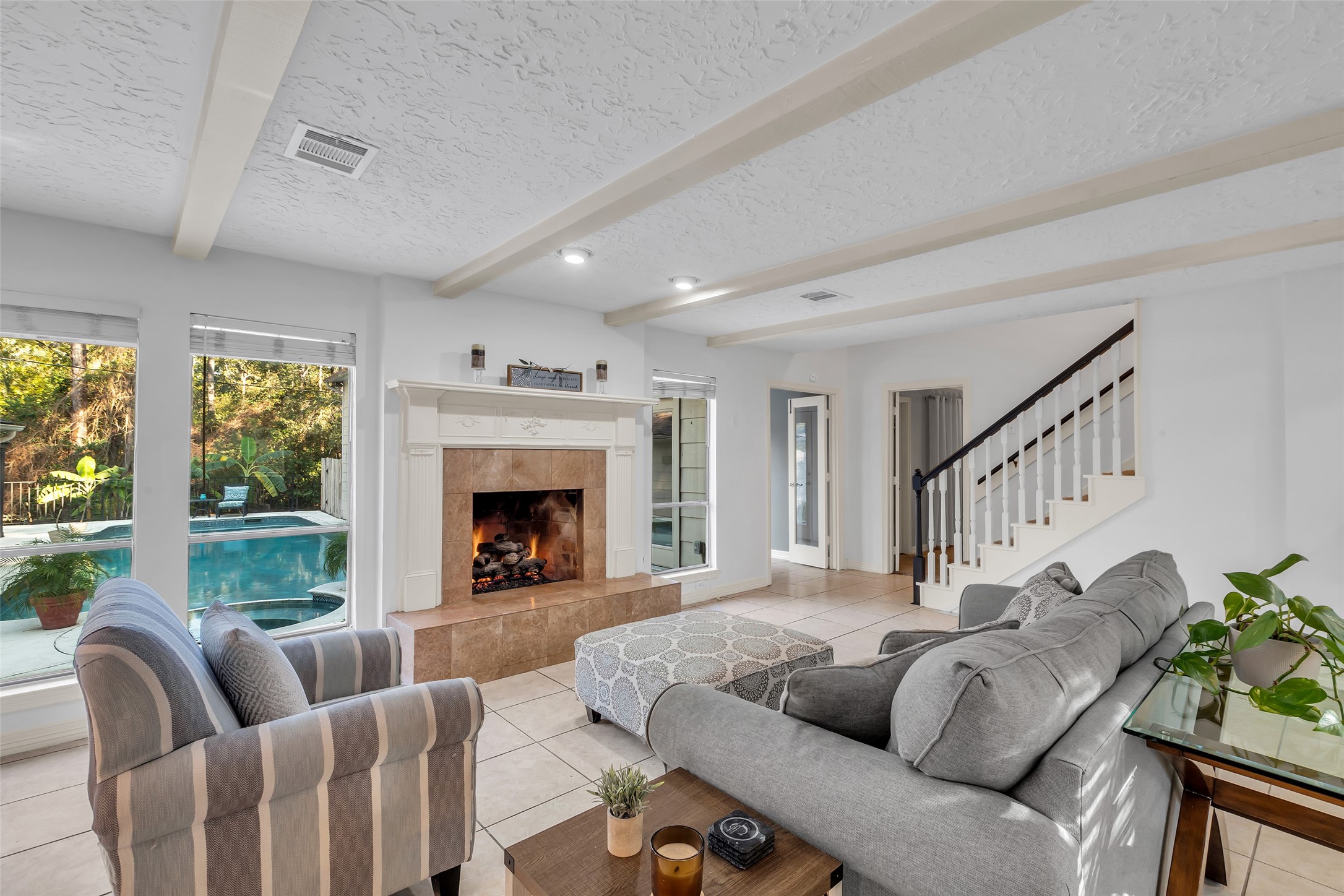 24102 Northcrest Drive Spring, TX 77389 - Photo 4 of 31 This inviting living room features a cozy fireplace, large windows overlooking a pool, and a staircase leading to the upper floor. The space is bright and airy, with comfortable seating and modern decor.