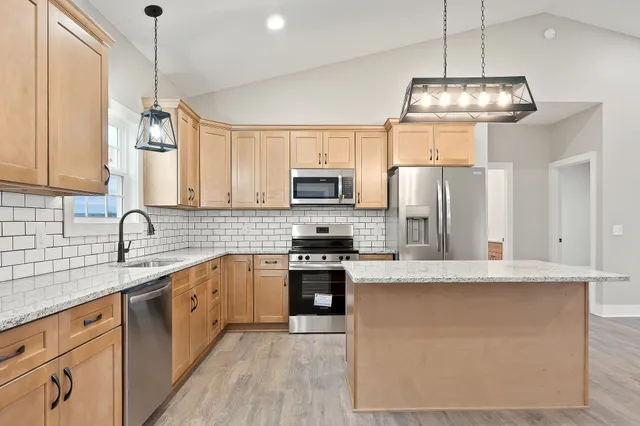 a kitchen with stainless steel appliances granite countertop a sink a stove a refrigerator cabinets and chairs