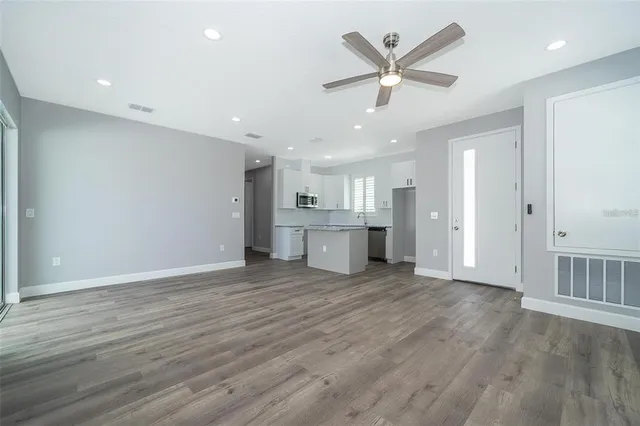 an empty room with wooden floor a ceiling fan and kitchen view