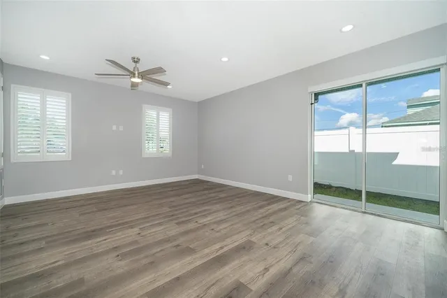 an empty room with wooden floor fan and windows