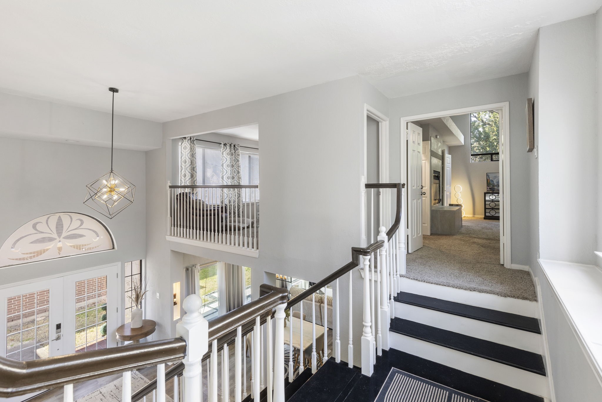 2110 Paso Rello Drive Houston, TX 77077 - Photo 32 of 41 This photo showcases a bright, open entryway with a stylish hanging light fixture. The staircase is accented with elegant white railings and dark wood handrails. The space leads to a cozy, carpeted study area with large windows, providing ample natural light.