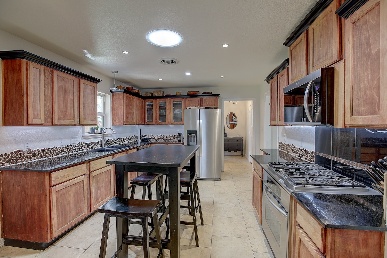1902 East 18th Street Georgetown, TX 78626 - Photo 20 of 40 Kitchen featuring stainless steel appliances, wood finish cabinetry, glass insert cabinets, dark stone counters, and light tile patterned floors