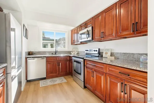 a kitchen with stainless steel appliances granite countertop a refrigerator a sink dishwasher and wooden cabinets with wooden floor