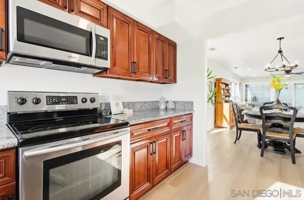 a kitchen with stainless steel appliances granite countertop a refrigerator a stove a dining table and chairs with wooden floor