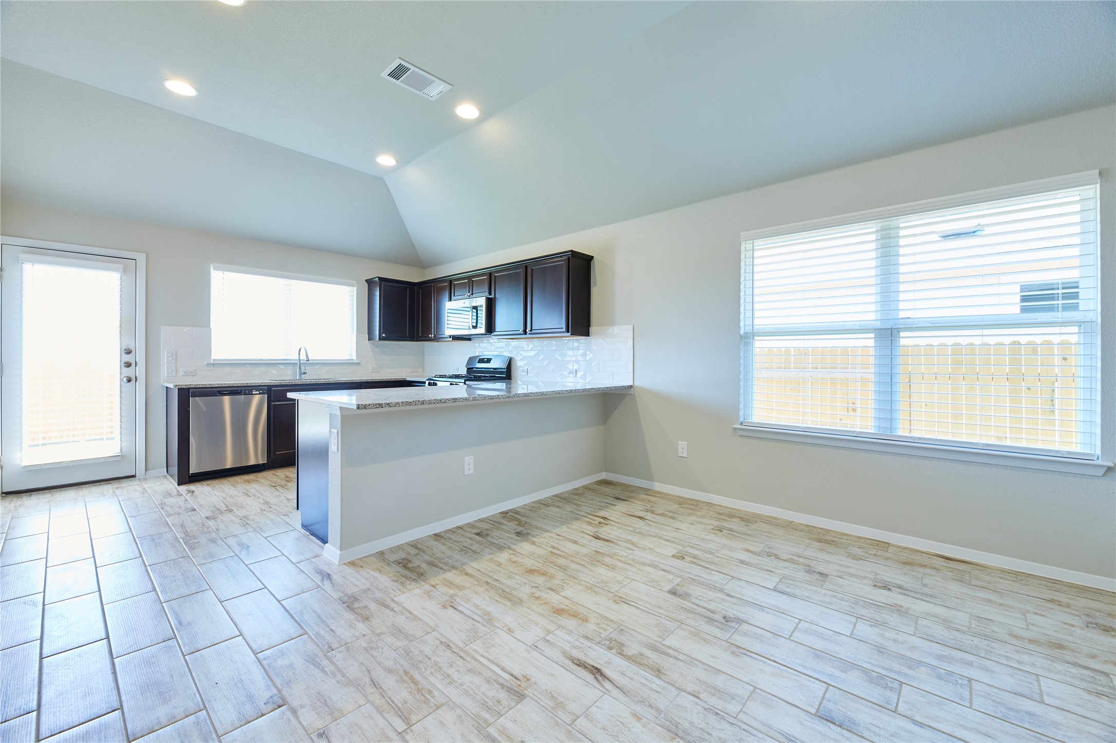 303 Trailside Lane Bastrop, TX 78602 - Photo 6 of 25 Kitchen with a peninsula, backsplash, vaulted ceiling, appliances with stainless steel finishes, and wood tiled floors