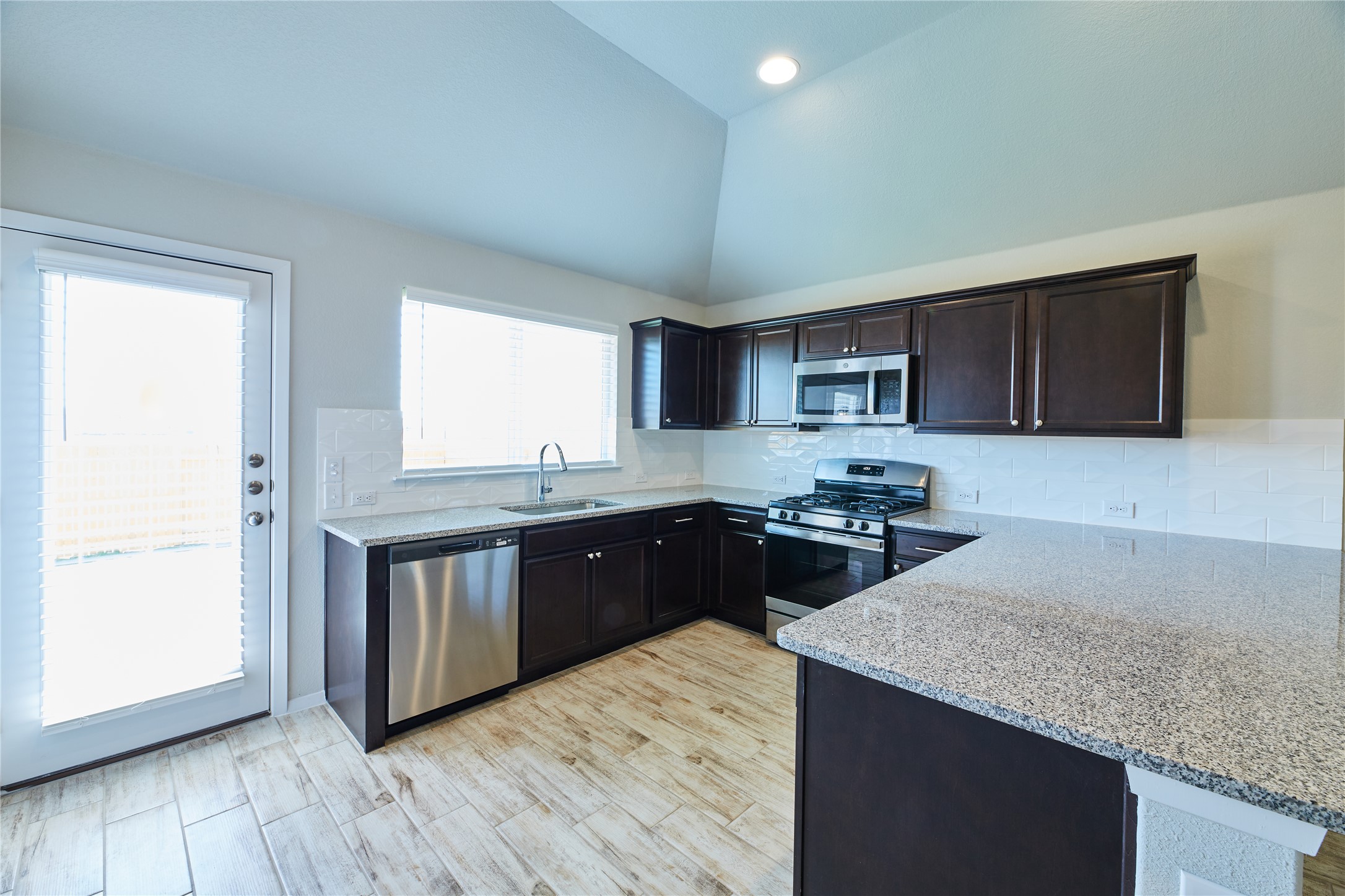 303 Trailside Lane Bastrop, TX 78602 - Photo 8 of 25 Kitchen featuring stainless steel appliances, tasteful backsplash, light stone counters, dark brown cabinetry, and light wood-style flooring