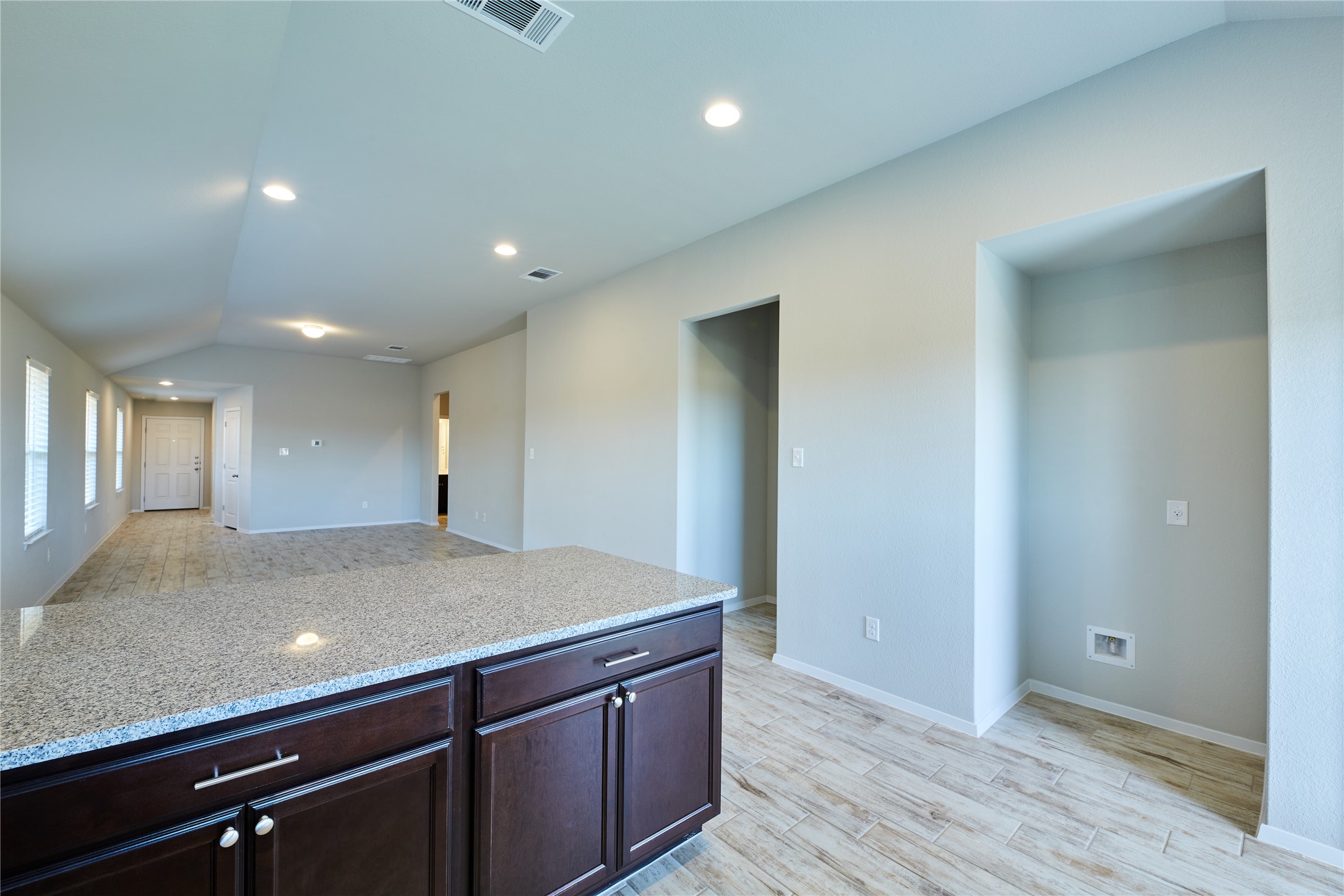 303 Trailside Lane Bastrop, TX 78602 - Photo 9 of 25 Kitchen with lofted ceiling, dark brown cabinets, light stone countertops, recessed lighting, and light wood finished floors