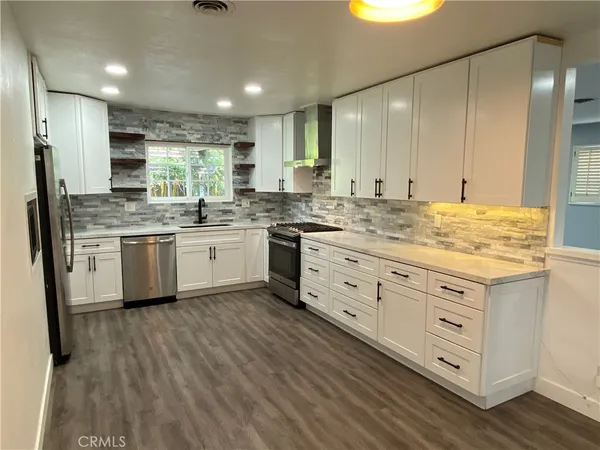 a kitchen with stainless steel appliances granite countertop a stove a sink and white cabinets with wooden floor